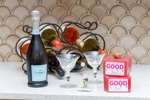 Bottle of La Marca Prosecco, two crystal glasses, lip balm, and pink Prosecco soap bars.