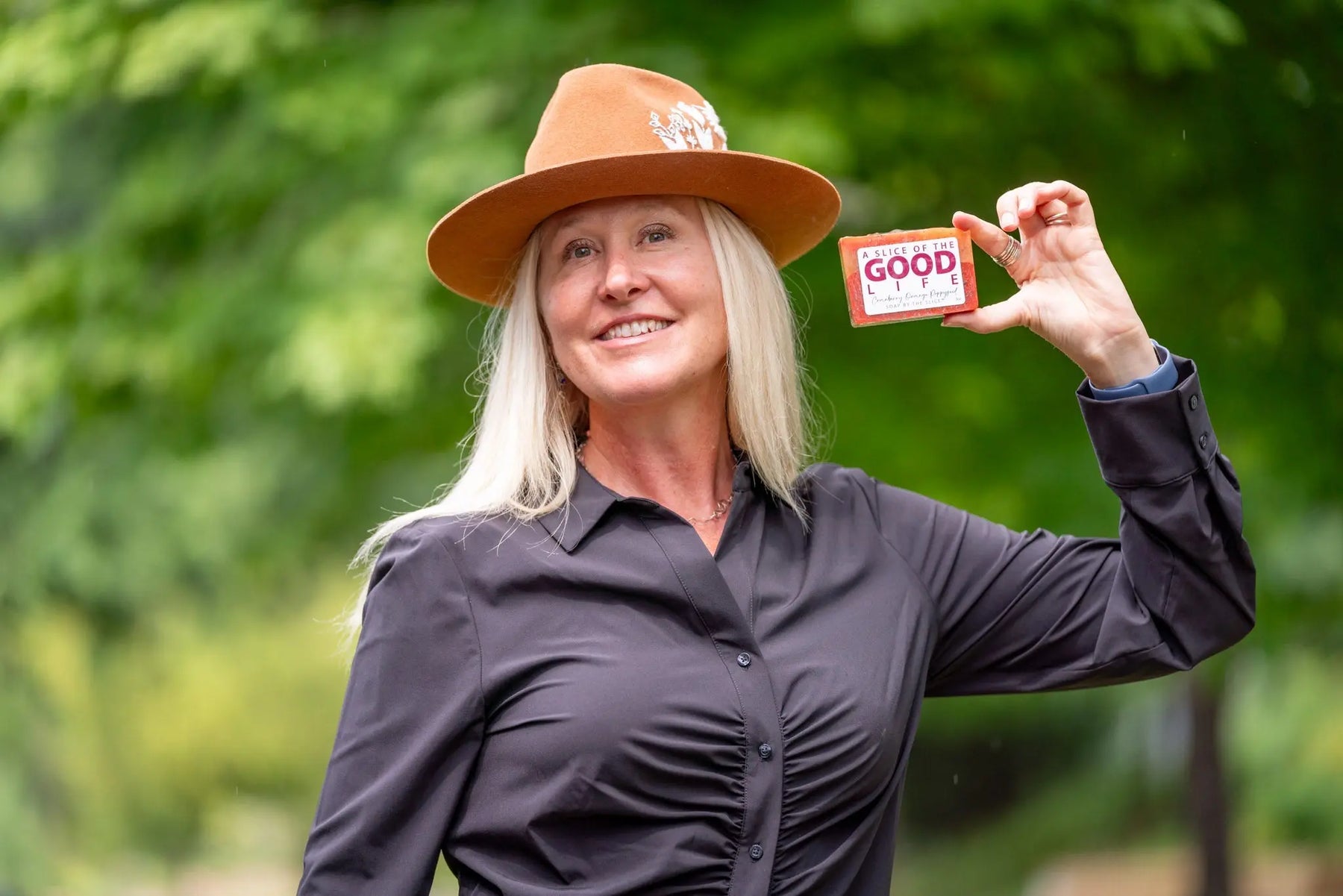 Woman holding a bar of cranberry orange poppyseed soap with 'A Slice of the Good Life' label.