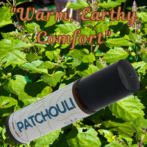 Patchouli roll-on oil with black cap shown against green leafy plant background. The label reads \"PATCHOULI ROLL-ONS\".