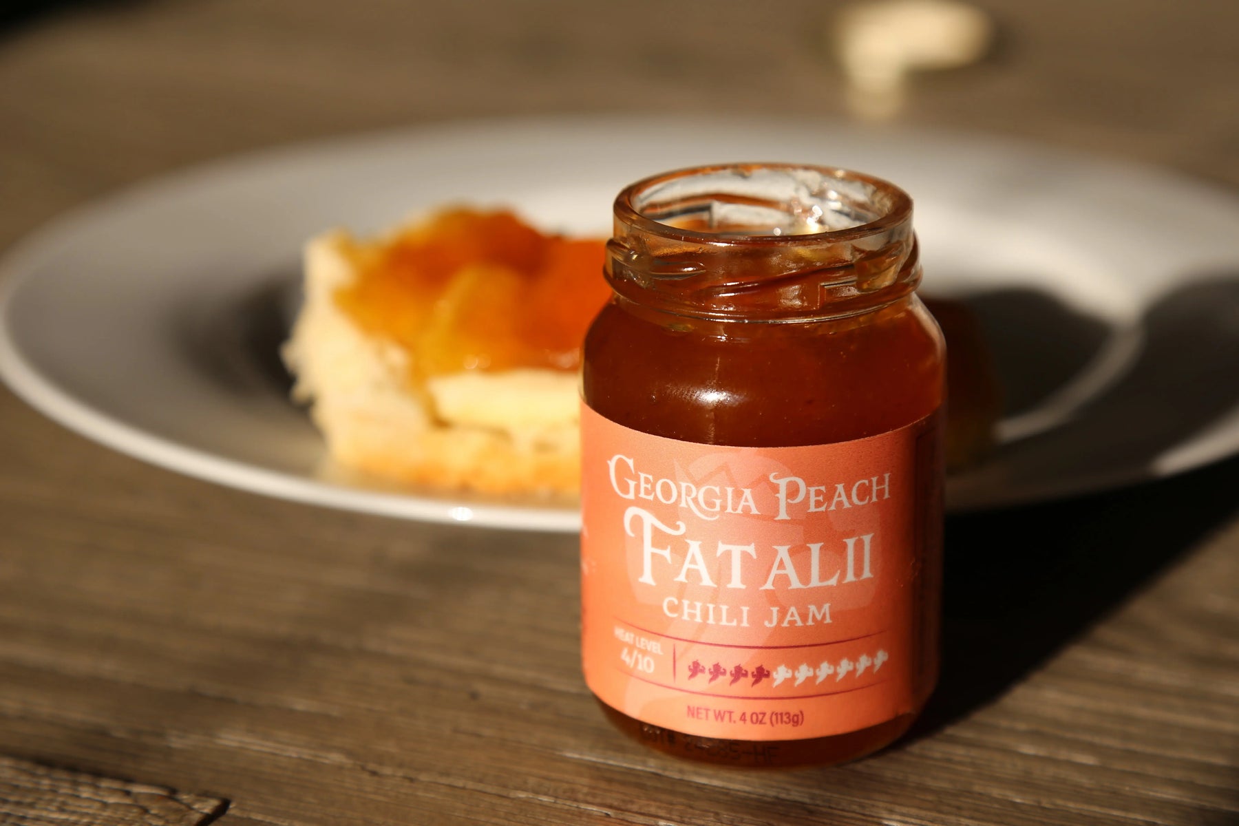 Georgia Peach Fatalii Chili Jam in a glass jar with a piece of pastry on a plate.