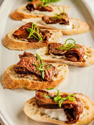 Beef steak crostini with whipped cheese and scallion garnish on a platter.
