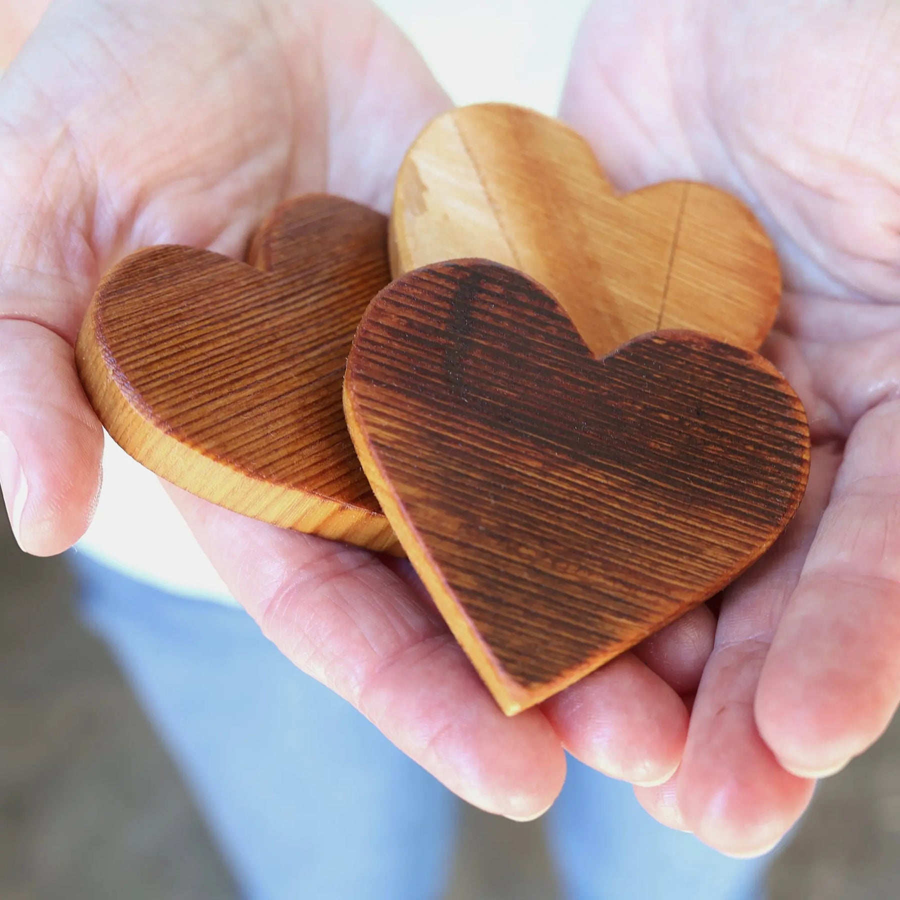 Three rustic wooden heart shapes held in cupped hands.