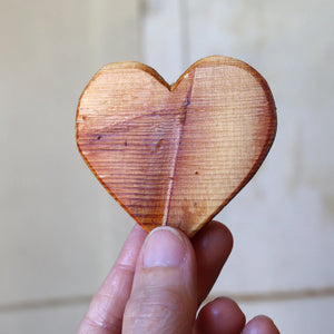 Wooden heart shape from reclaimed piano soundboard held by fingers