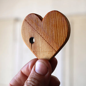 Hand holding a handmade wooden heart with a hole.