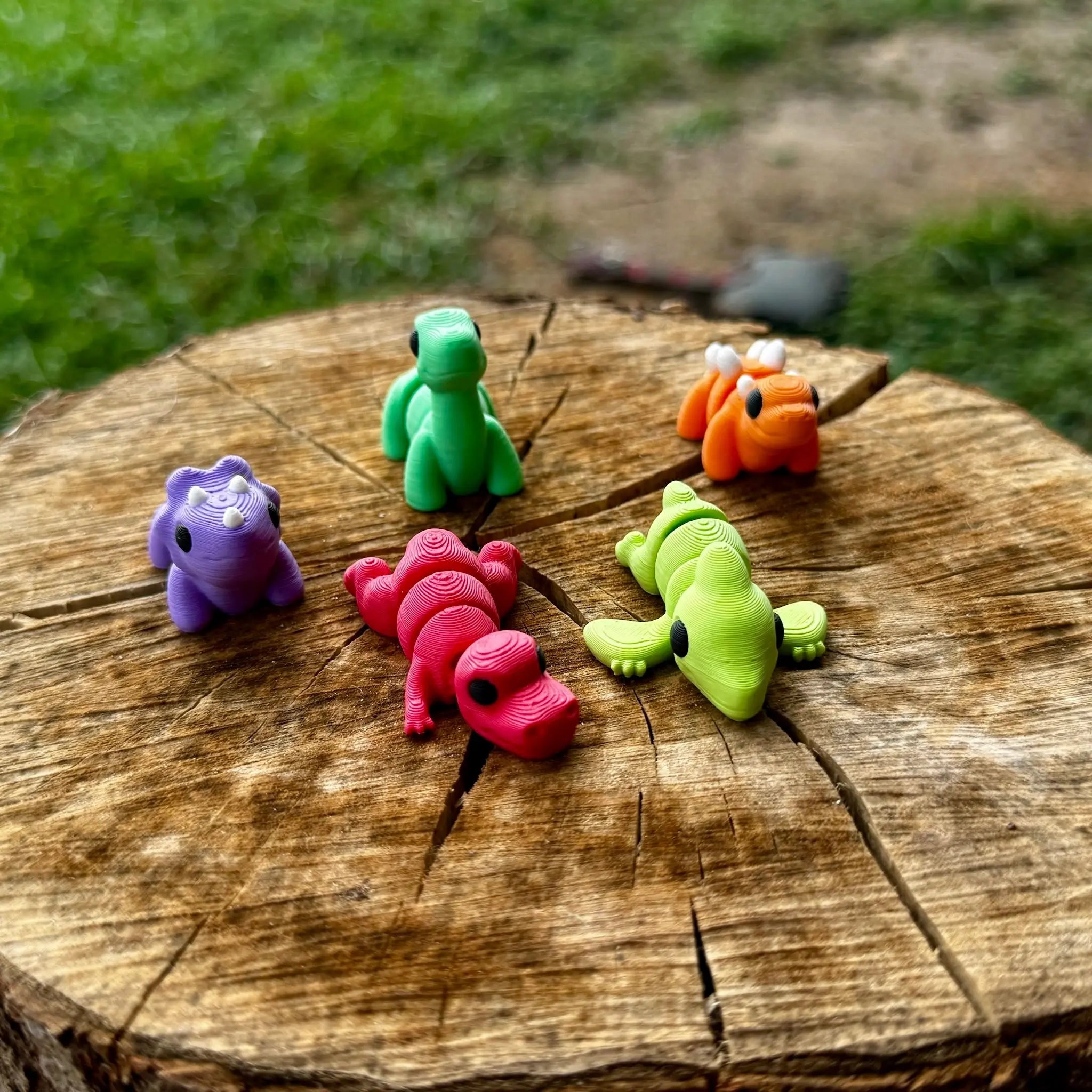 3D printed dinosaurs toys on tree stump: Brontosaurus, Pterodactyl, Stegosaurus, T-Rex, Triceratops.