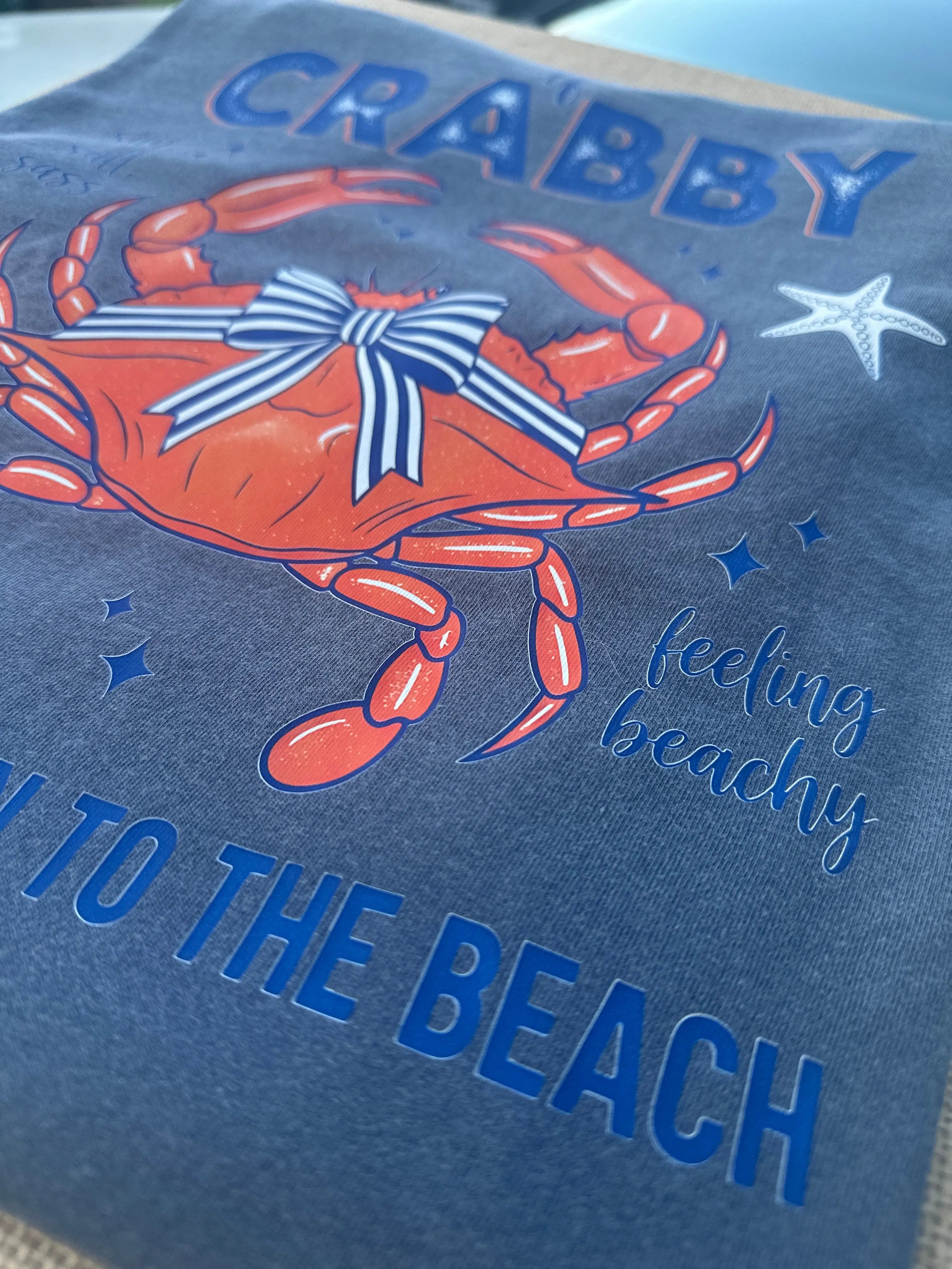 Blue t-shirt with a graphic of an orange crab and the text "Feeling Beachy" and "To The Beach".