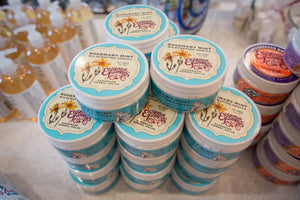 Stack of Rosemary Mint Arnica herbal salve jars with blue and teal labels.