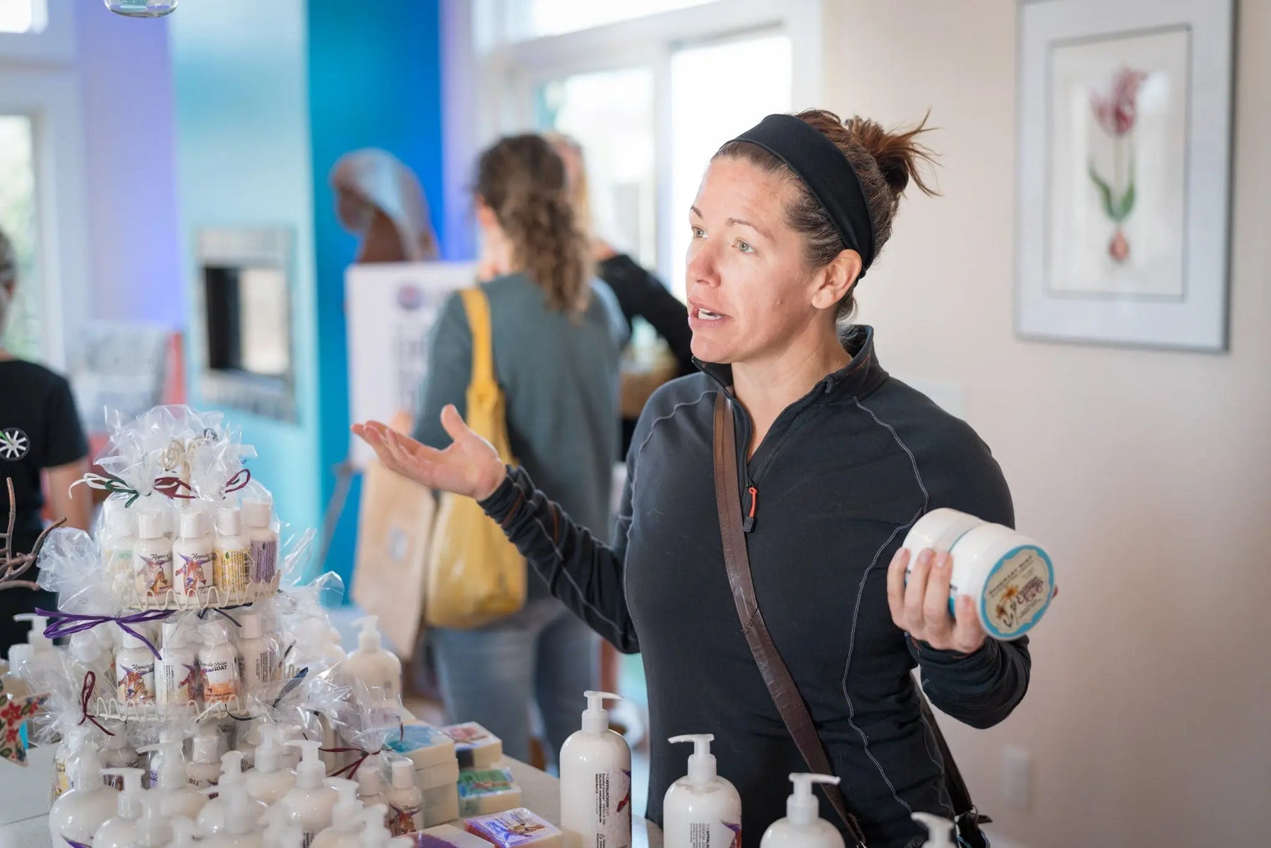 Woman presenting ROSEMARY MINT ARNICA SALVE 8 oz. Essential Journeys product at a table.