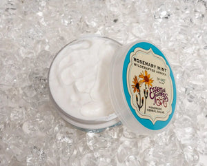 Essential Journeys Rosemary Mint Arnica Salve in clear jar with blue label on ice.