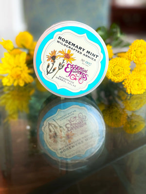 Tin of Rosemary Mint Wildcrafted Arnica Herbal Salve surrounded by yellow flowers.