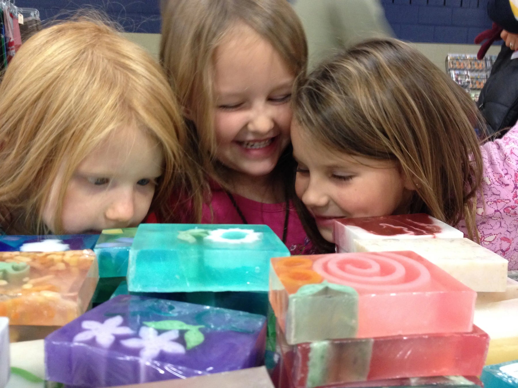 Three children looking at colorful handmade soaps with floral and swirl patterns.
