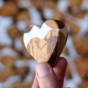 Heart-shaped reclaimed olive wood and white resin object held by a thumb