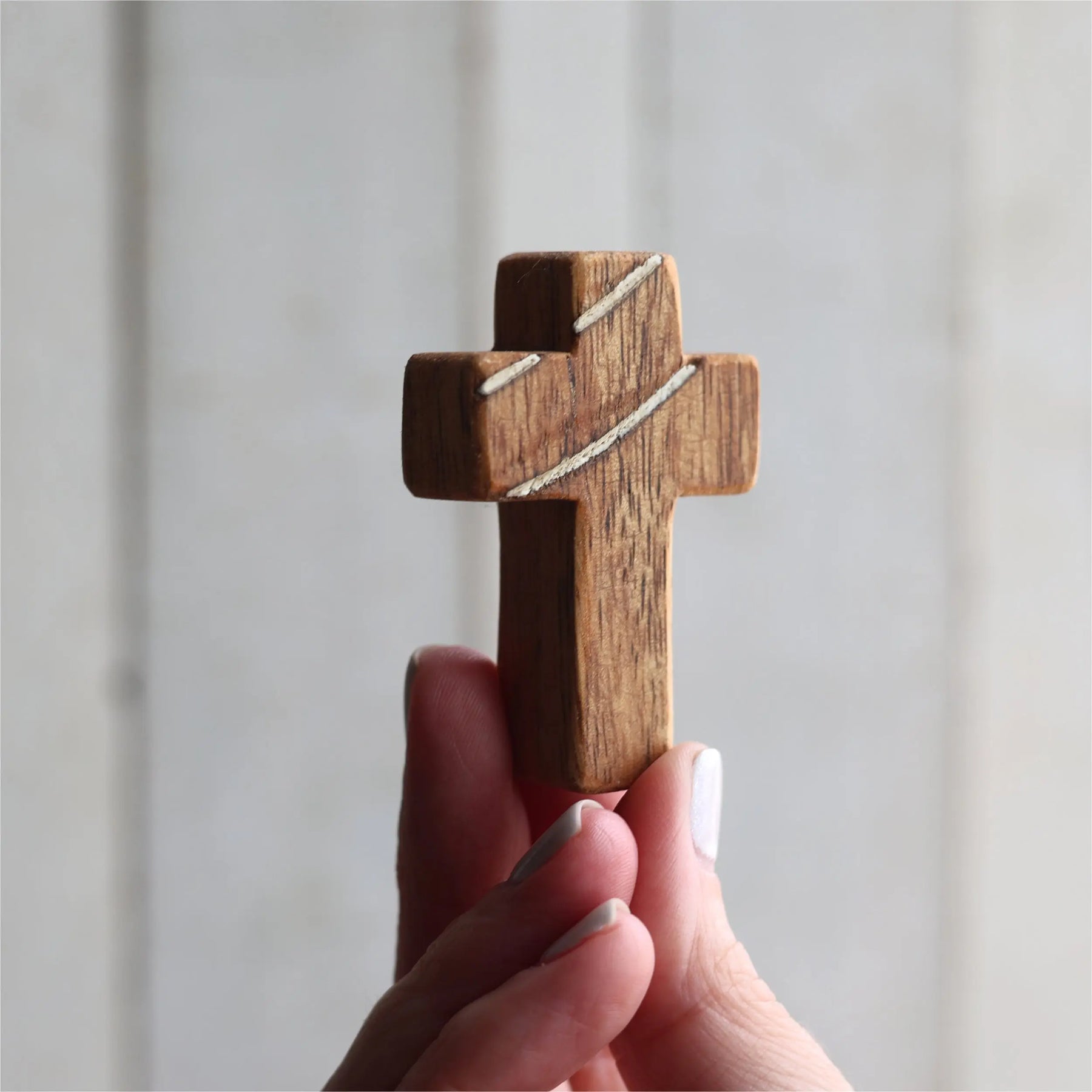 Handheld wooden cross with decorative inlays on a light background.