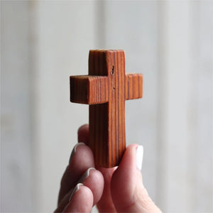Wooden cross held in a hand with visible wood grain and texture.