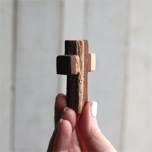 Reclaimed wood pocket cross held in a hand with white painted fingernails.