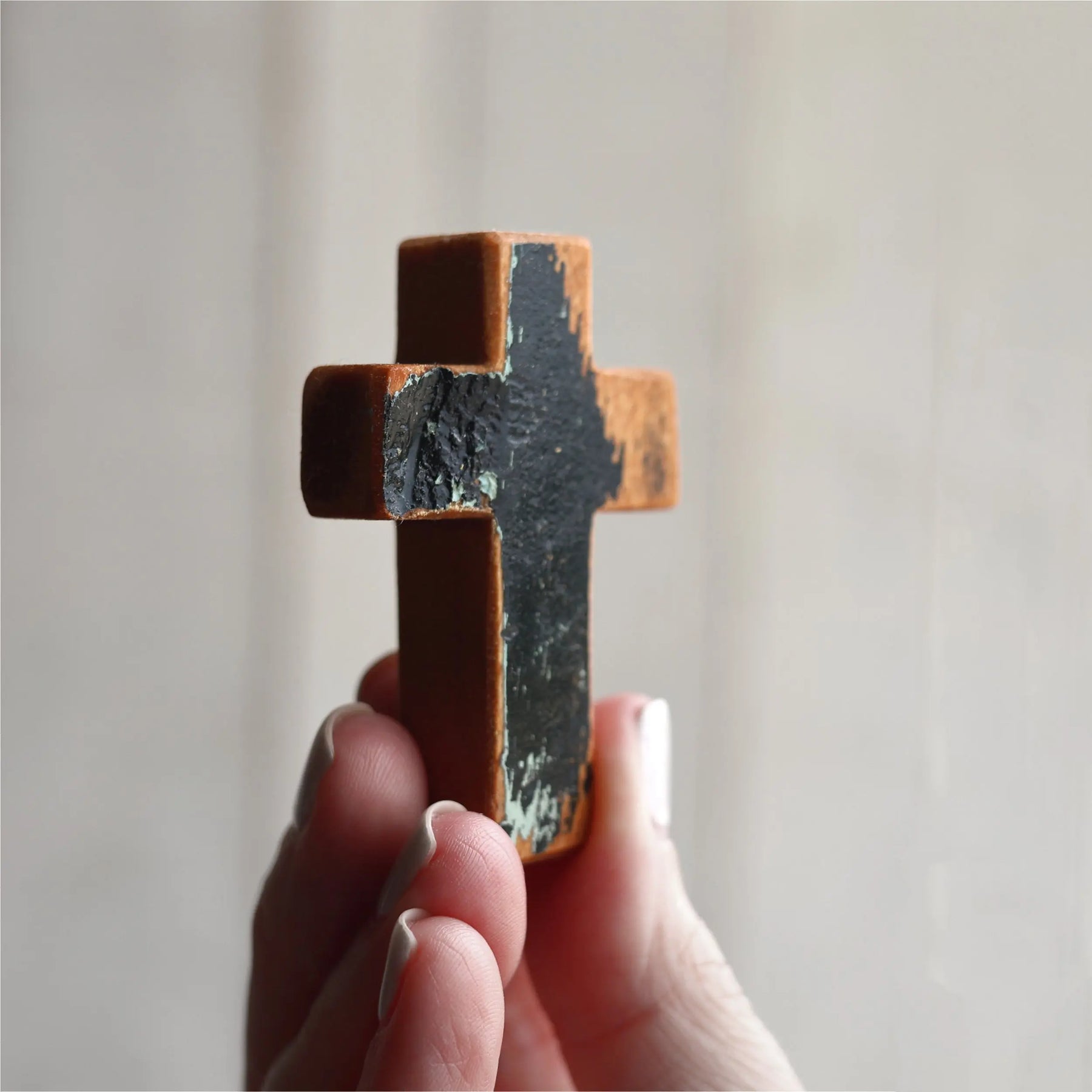 Wooden pocket cross with textured dark finish held by a hand.