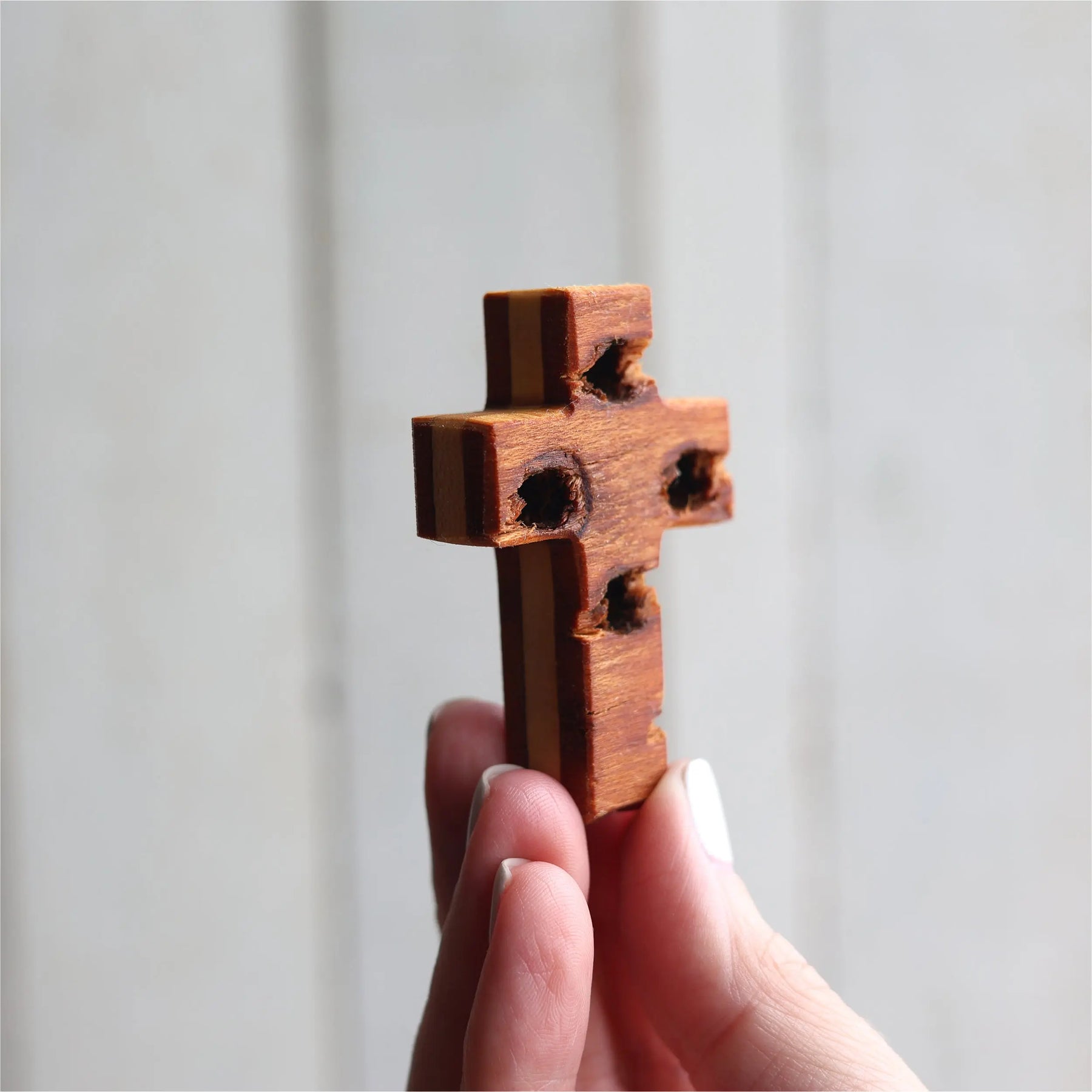 Wooden rugged pocket cross with visible holes and rough texture.