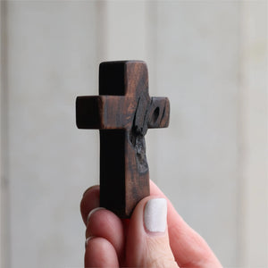 Dark wooden pocket cross held in a hand, showing rustic texture