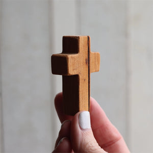 Hand holding a small, brown wooden cross with a matte finish.