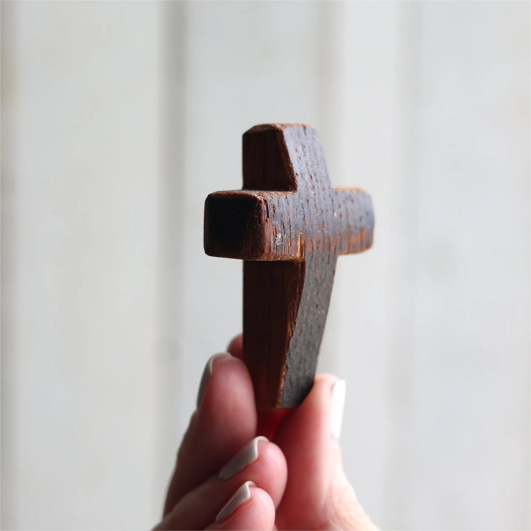 Close-up of a dark wooden pocket cross held between fingers against a light background.