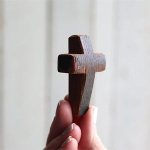 Close-up of a dark wooden pocket cross held between fingers against a light background.