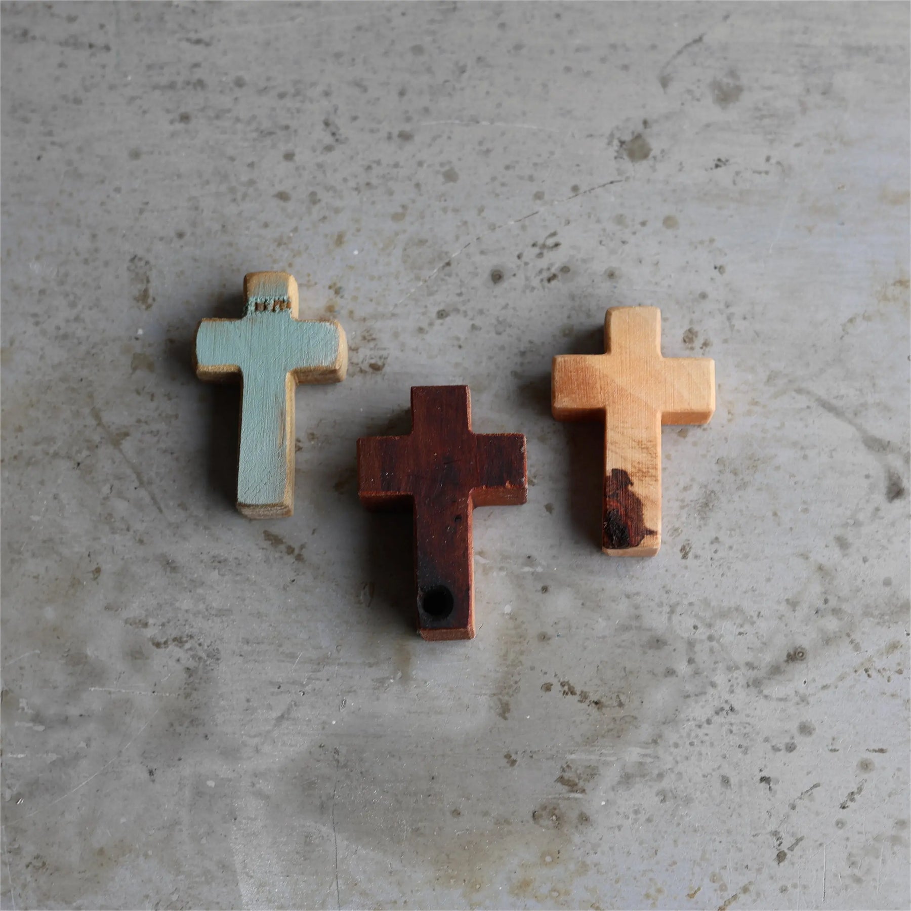 Three wooden pocket crosses: one teal, one dark brown, and one light wood.