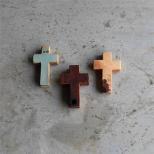 Three wooden pocket crosses: one teal, one dark brown, and one light wood.