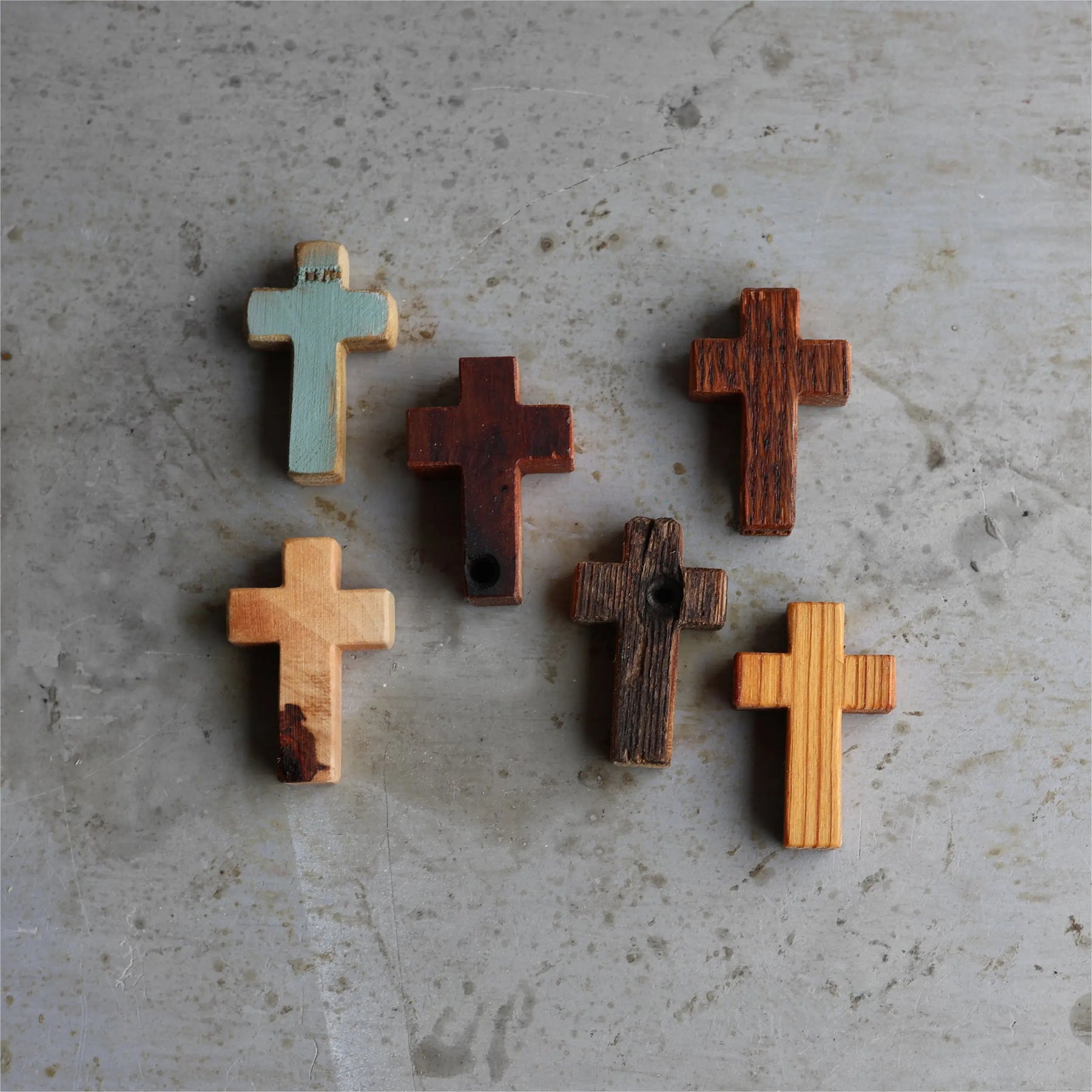Six wooden pocket crosses with varied textures and finishes on a textured surface.