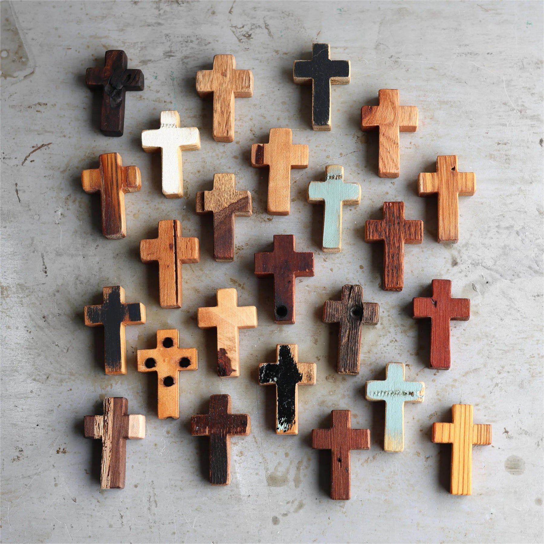 Collection of wooden pocket crosses with varied wood grains and colors arranged on a textured surface.