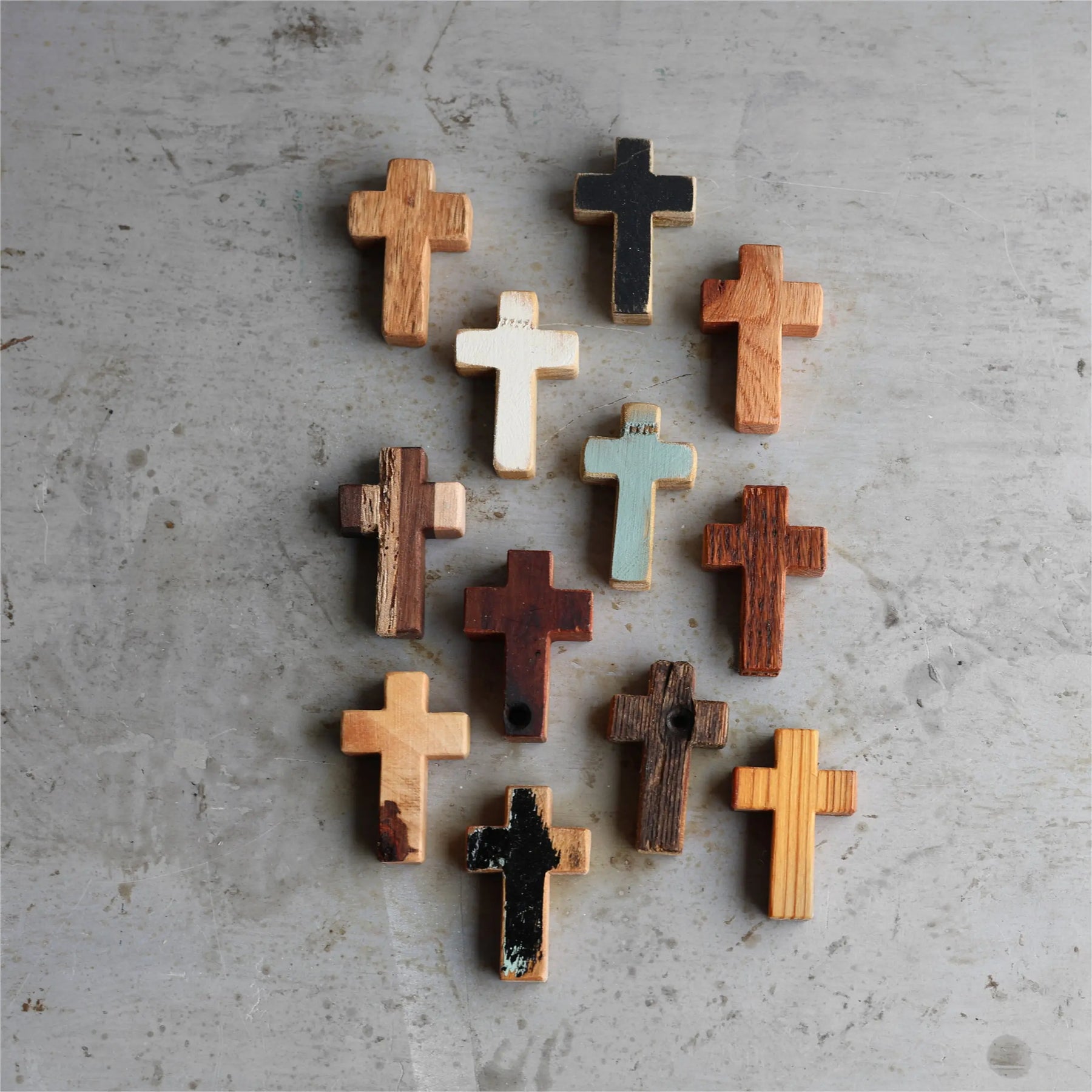 Group of varied wooden crosses with different textures and colors on a textured gray surface.