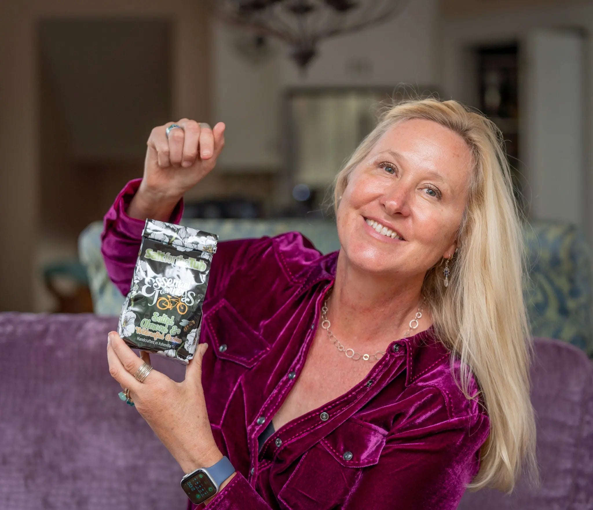 Woman holding Salted Almond & Arnica bath salts package with floral design.
