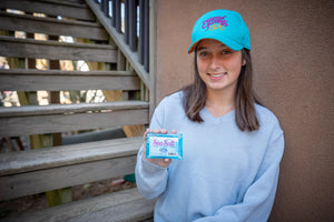 Woman in blue sweater and teal cap holding a bar of Sea Salt hand and body soap