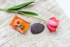 Orange sunflower soap slice, stone with "HAPPINESS," and pink tulip on textured cloth.