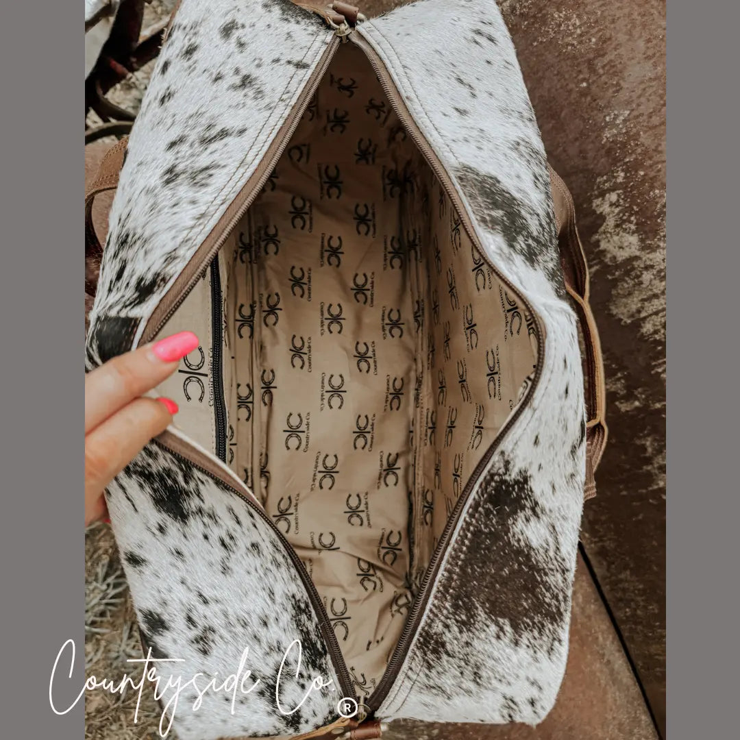 Open cowhide duffle bag with patterned interior lining and leather straps.