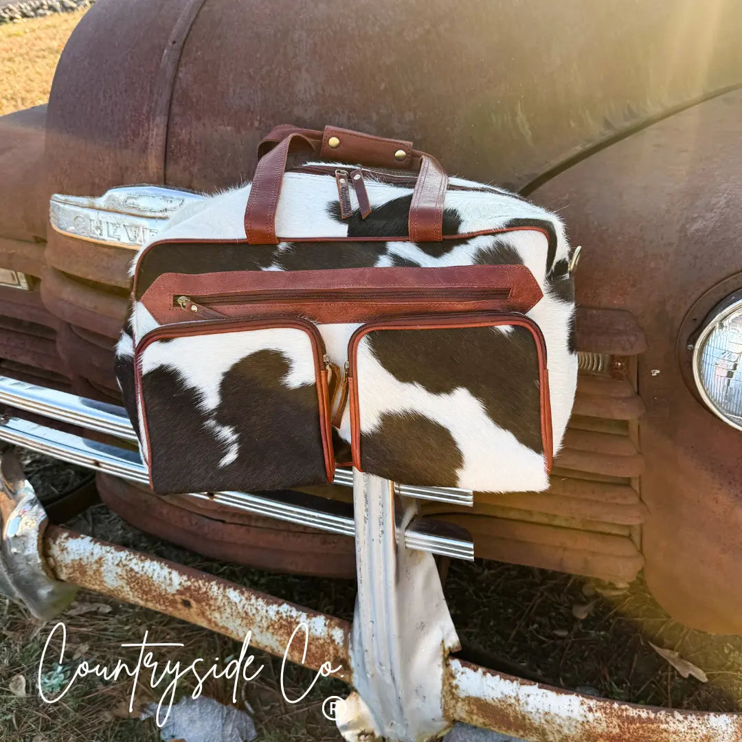 Cowhide duffle travel bag with leather accents on a vintage truck.