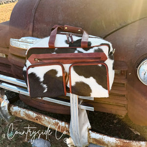 Cowhide duffle travel bag with leather accents on a vintage truck.