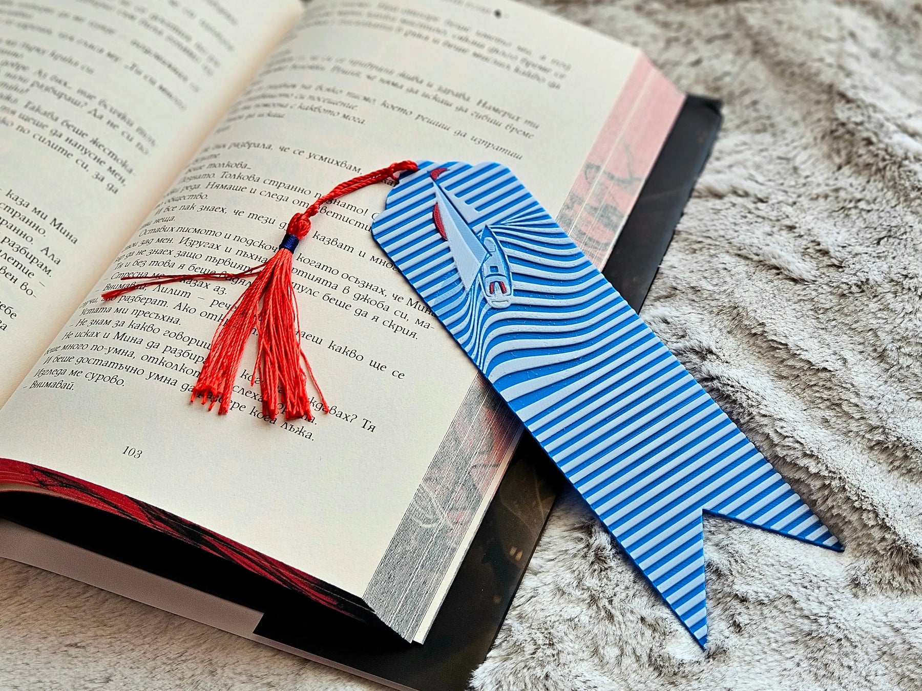Nautical bookmark with sailboat and blue ocean waves design with a red tassel in an open book.