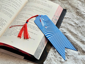 Nautical bookmark with sailboat and blue ocean waves design with a red tassel in an open book.
