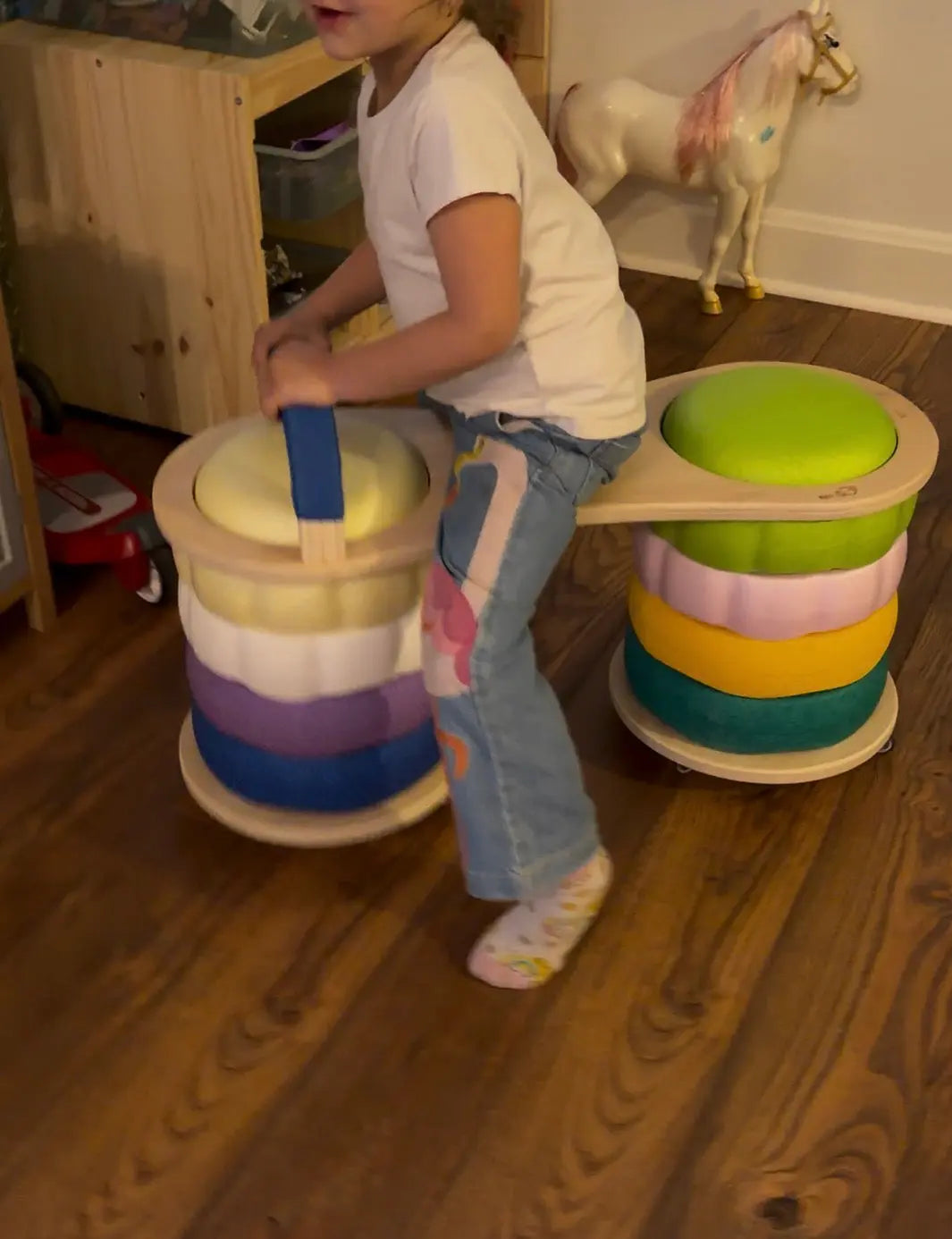 Child playing on a colorful wooden scooter board with a play horse in the background.