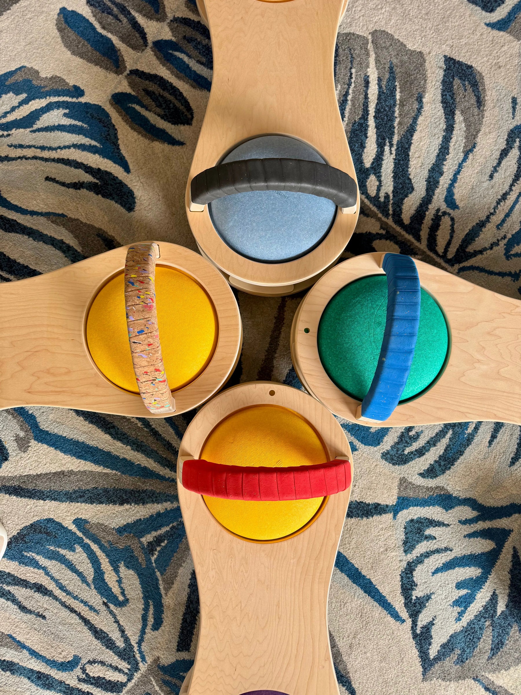 Four wooden scooter boards with multicolored handles arranged on a patterned rug.