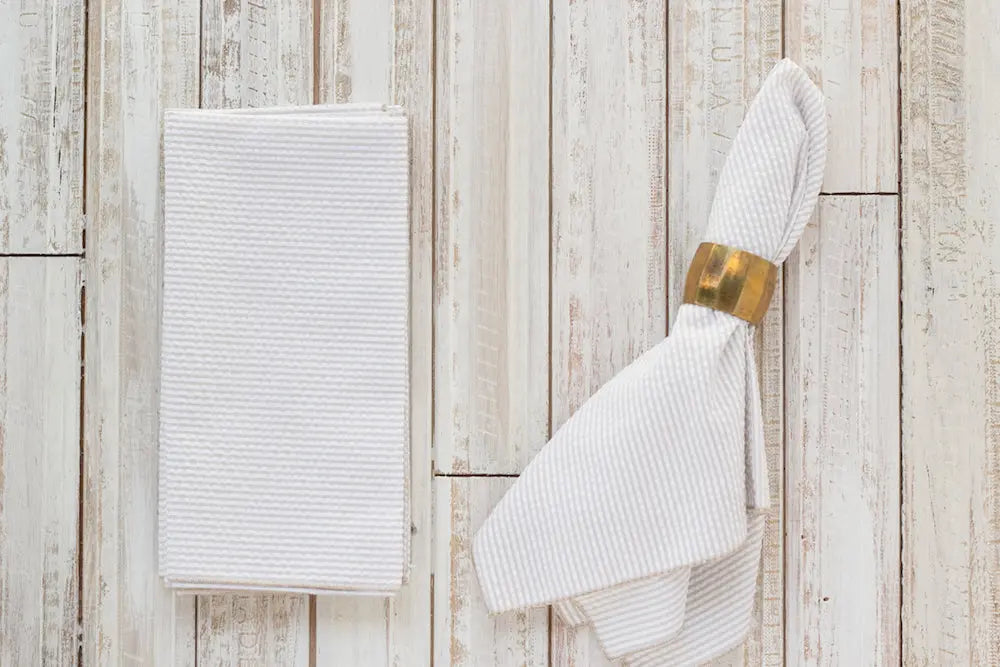 White seersucker cloth dinner napkins on a light wood background.