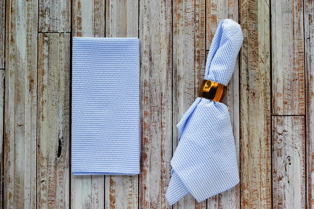 Light blue and white striped seersucker napkins and gold napkin ring on wood
