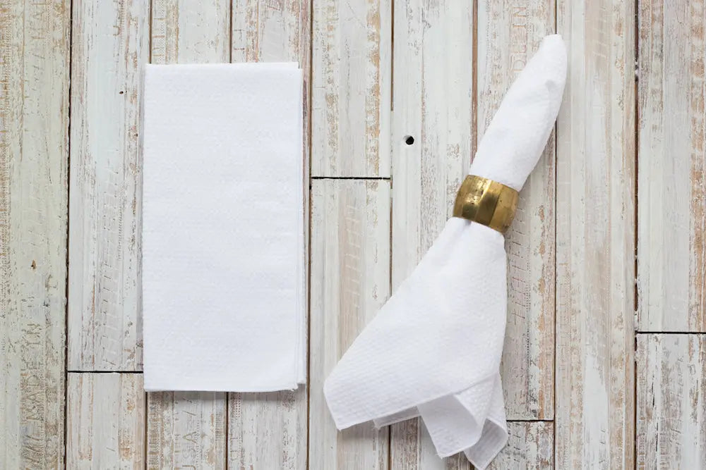 White seersucker cloth napkins with a brass napkin ring on a wood background.