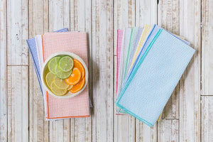 Seersucker napkins with fruit slices in a bowl on a white wooden background.
