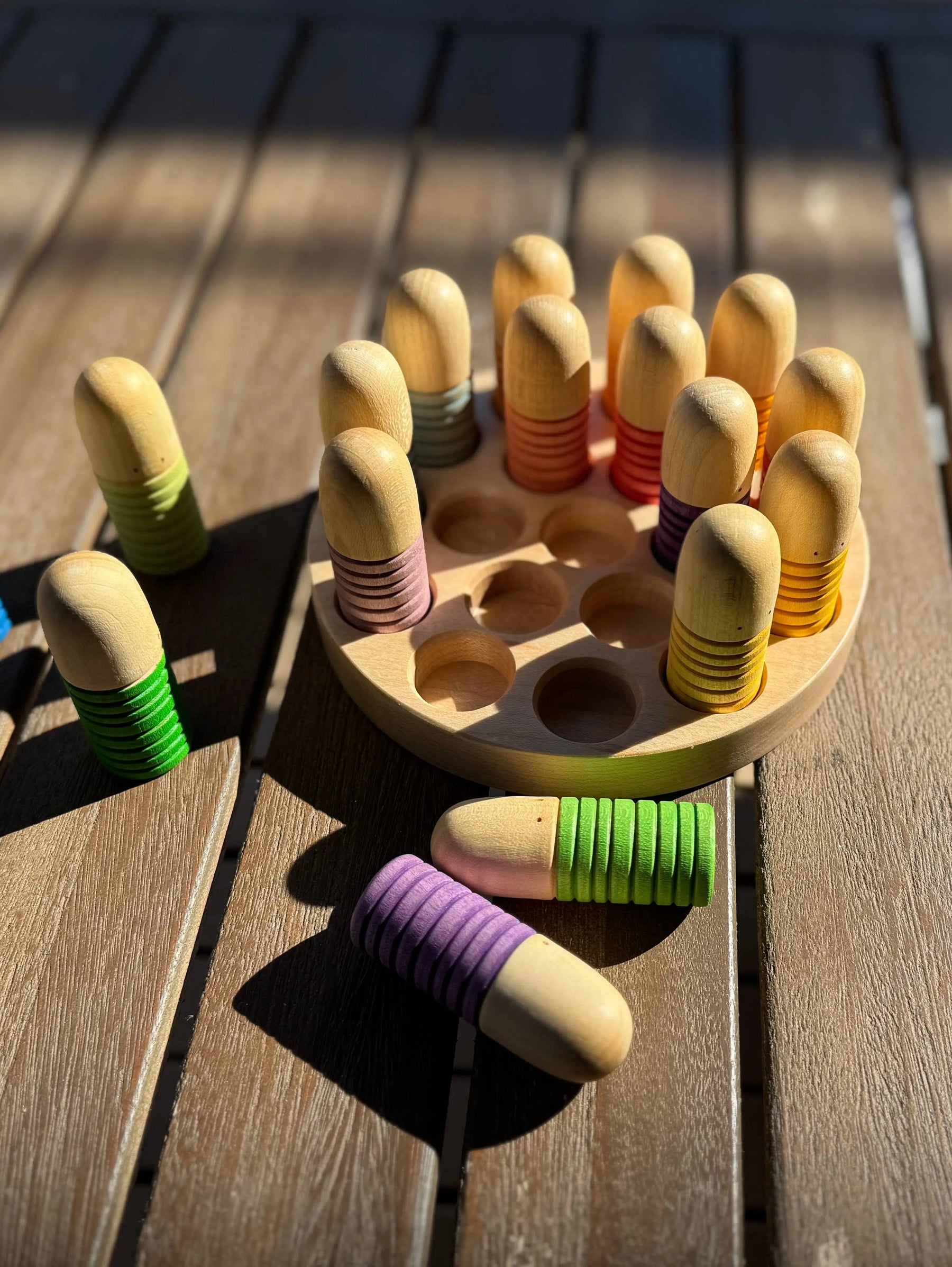 Wooden sorting tray with colorful pegs and holes on a wooden table.