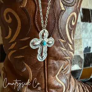 Silver-tone Southwestern cross necklace with turquoise stone on brown boot.