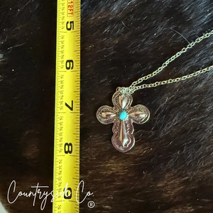 Silver Southwestern cross necklace with turquoise stone next to measuring tape.