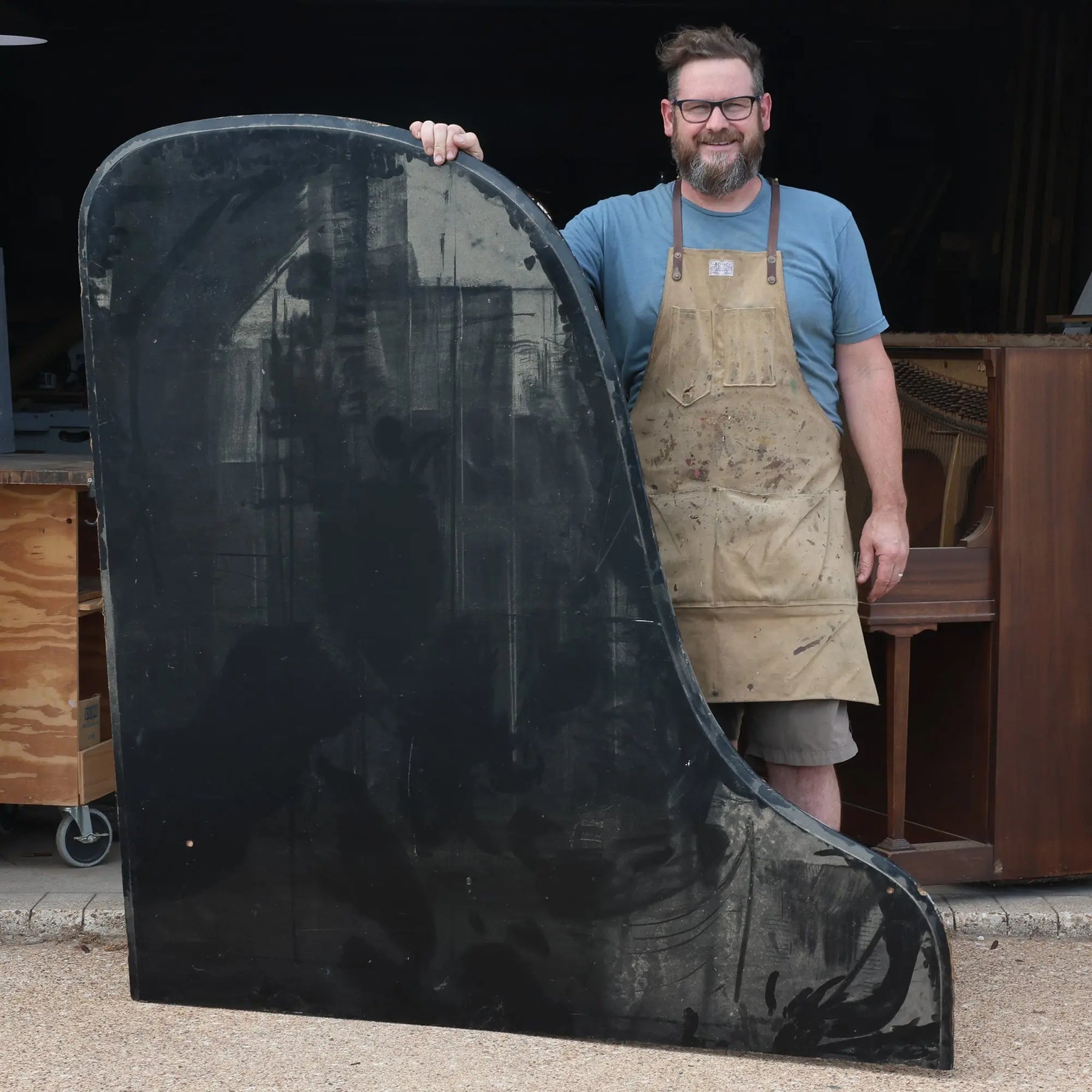 Man holding a large, curved, black piano soundboard piece.