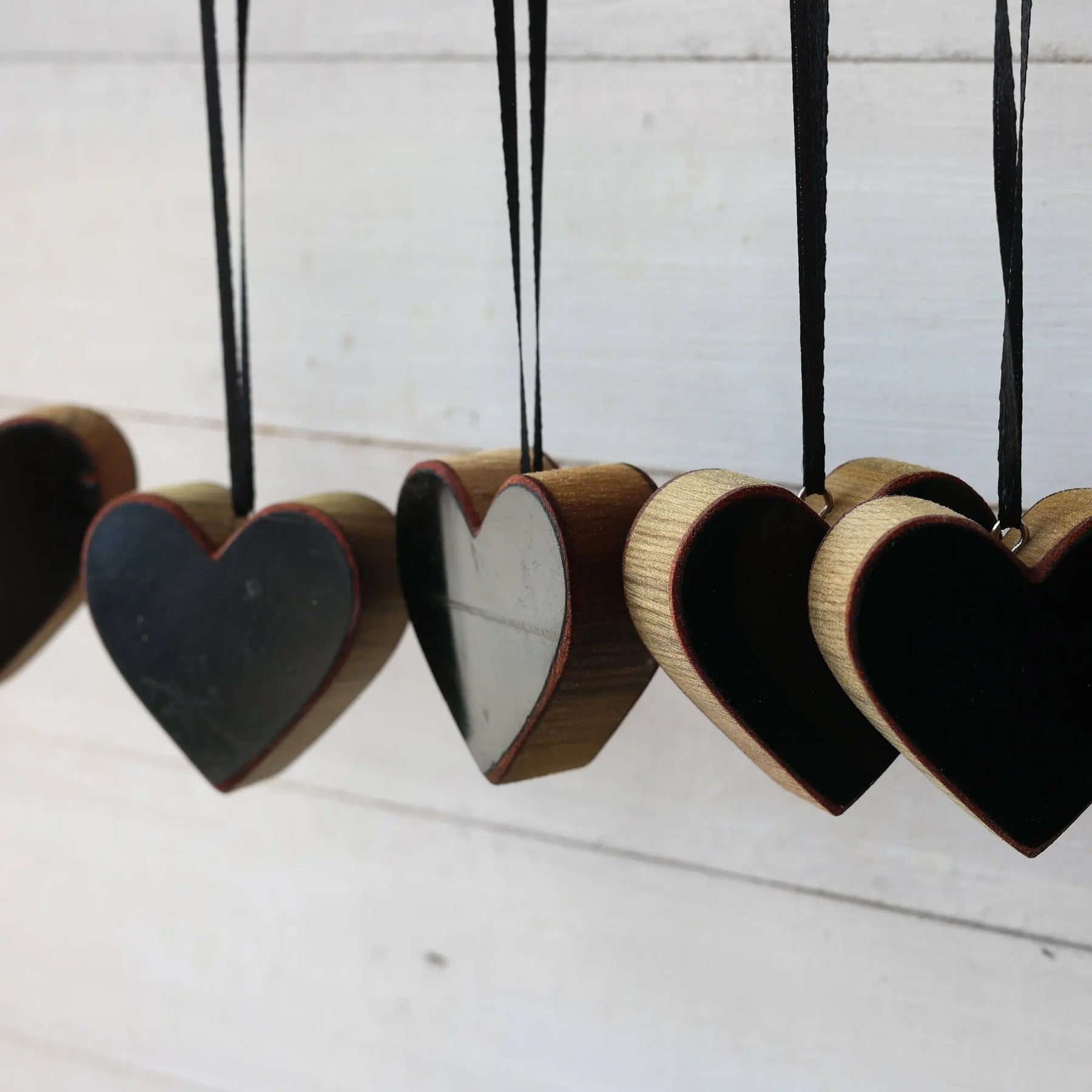 Row of wooden heart ornaments with black centers and black ribbon hangers.