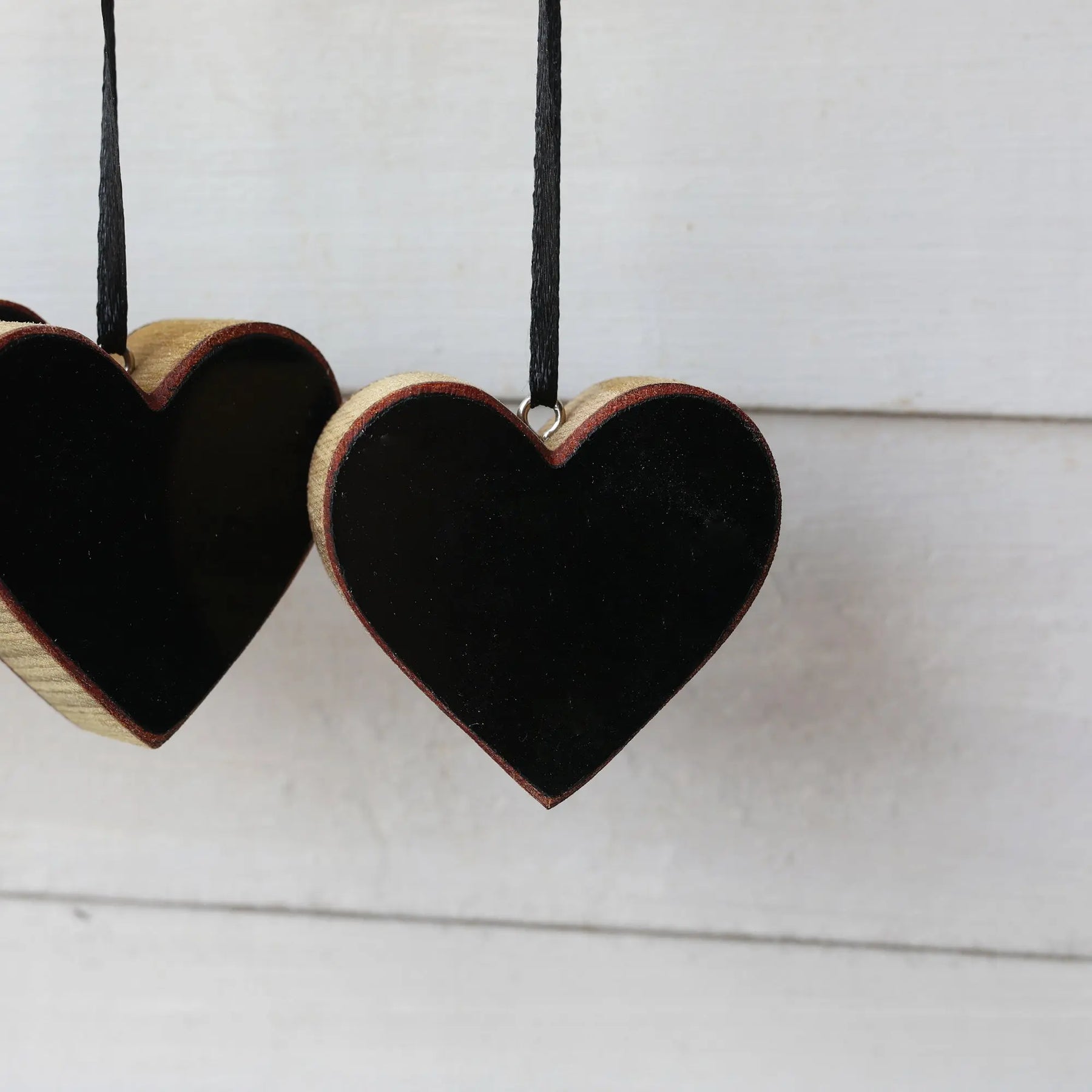 Wooden heart ornament with black inlay and black ribbon hanger against a white background.